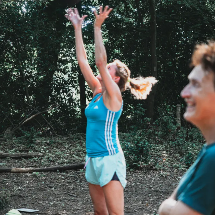 Vrouw springt actief omhoog tijdens buitensportles in het bos, sfeerbeeld bij groepslessen van Fitcoach Wilma