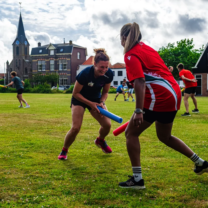 Twee vrouwen sporten actief buiten op het gras bij een trainingsonderdeel met een blauwe stok, bij Fit Coach Wilma