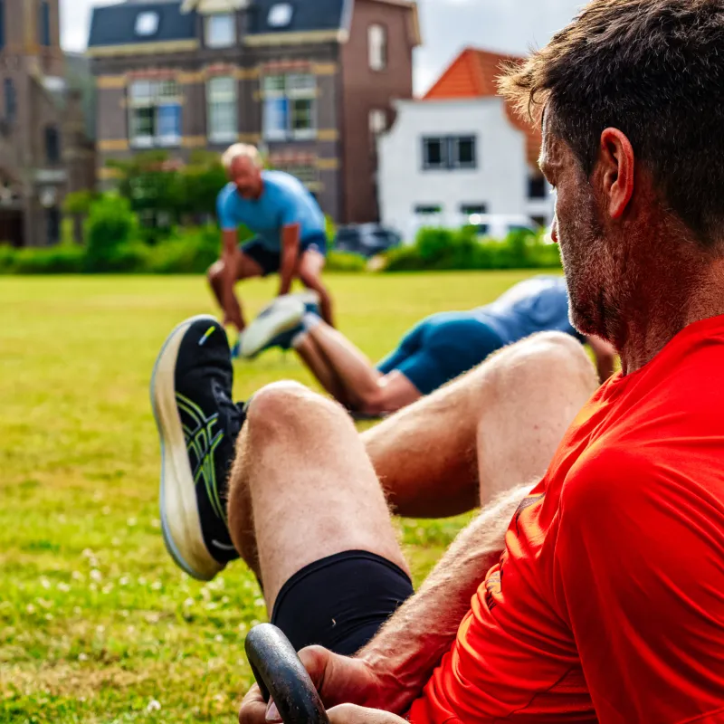Mannen doen buikspieroefeningen buiten op het gras tijdens een groepstraining in de zon